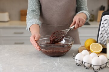 Woman mixing chocolate cream with whisk in bowl at gray marble table indoors, closeup