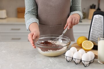 Woman making chocolate dough with whisk in bowl at gray marble table, closeup
