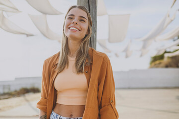 Young smiling cheerful fun cool minded calm woman she wearing orange shirt beige top casual clothes look aside in reverie mood rest relax walk outside in summer day. Urban lifestyle leisure concept. - obrazy, fototapety, plakaty