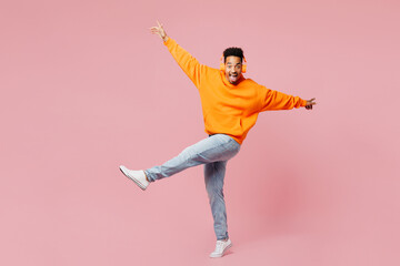 Full body side view young man of African American ethnicity wear yellow hoody casual clothes listen to music in headphones spread hand dance isolated on plain pastel pink background Lifestyle concept
