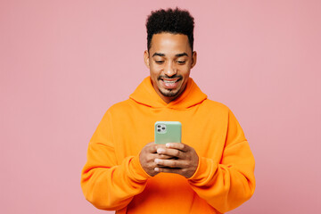 Young smiling happy man of African American ethnicity wear yellow hoody casual clothes hold in hand use mobile cell phone isolated on plain pastel pink background studio portrait. Lifestyle concept.