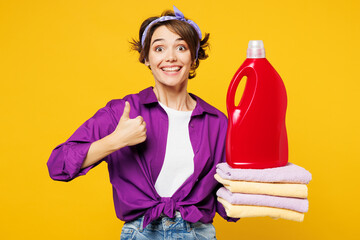 Young happy smiling woman wear purple shirt do housework tidy up hold pile of towels after laundry,...