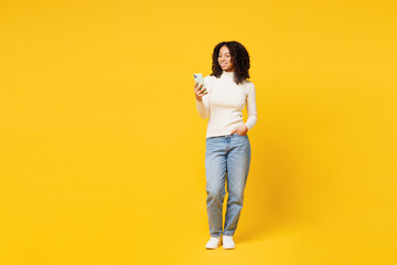 Fototapeta na wymiar Full body happy little kid teen girl of African American ethnicity wear white casual clothes hold in hand use mobile cell phone isolated on plain yellow background studio. Childhood lifestyle concept.