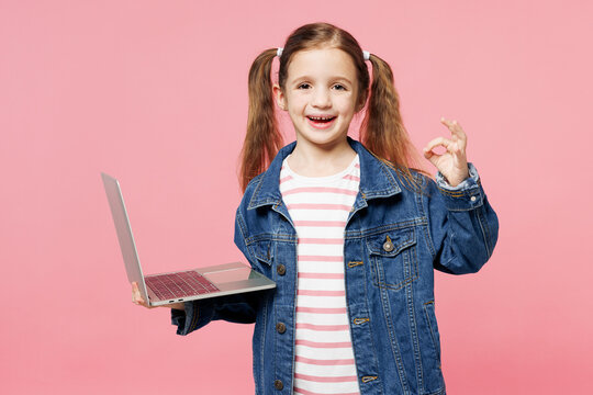 Little child kid IT girl 7-8 years old wears denim shirt have fun hold use work on laptop pc computer show ok okay isolated on plain light pink background. Mother's Day love family lifestyle concept.