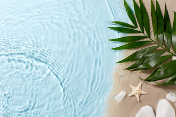 Tranquil beach retreat: Overhead view of green palm leaves, starfish, and white stones on sand and blue water background with space for text or message