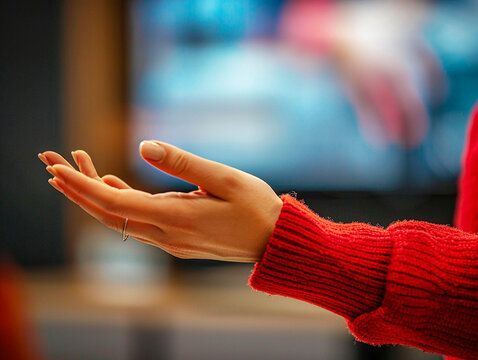 A close-up of the managers hands as she gestures during her presentation with a blurred background of the TV set