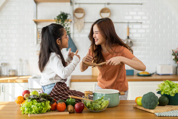 Portrait of enjoy happy love asian family mother with little asian girl daughter child help cooking food healthy eat with fresh vegetable testing smell soup in a pot with spoon in kitchen at home