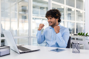 A joyful business professional in an office, celebrating success with a fist pump. A moment of triumph and happiness captured.