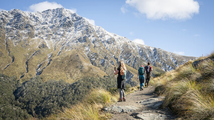 Fototapeta na wymiar Hikers walking towards snowy mountain during sunny autumn day, New Zealand