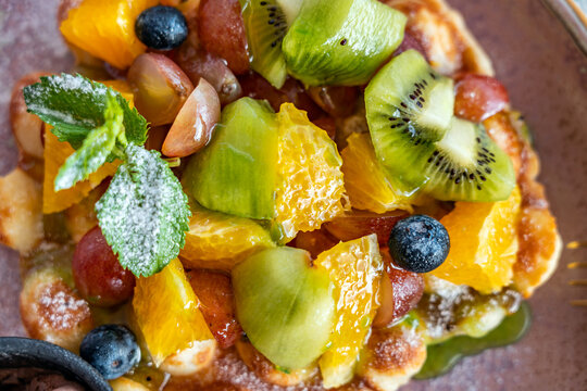 Delicious fruit dessert with pastry in powdered sugar on a plate close-up. Top view