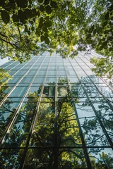 Foto auf Glas Sustainable green building. Eco-friendly building. Sustainable glass office building with tree for reducing carbon dioxide. Office with green environment. Corporate building reduce CO2. © Artinun