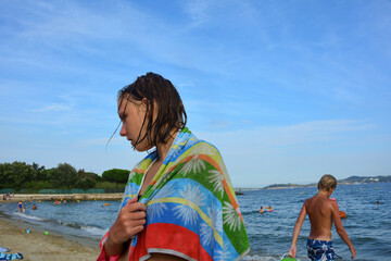 Girl with a towel on the beach, a boy standing behind