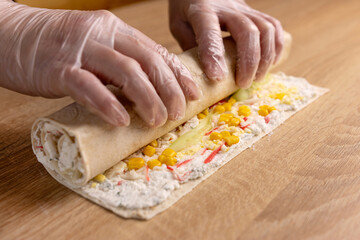 Lavash with filling and vegetables is wrapped in a roll. Preparation of pita bread roll.