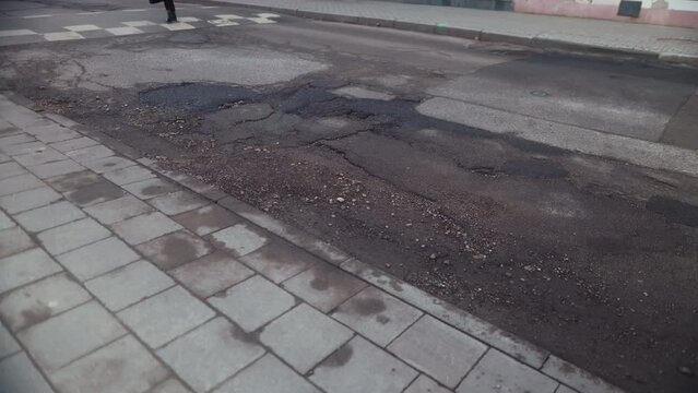 Person navigating uneven road surface with numerous potholes on narrow street
