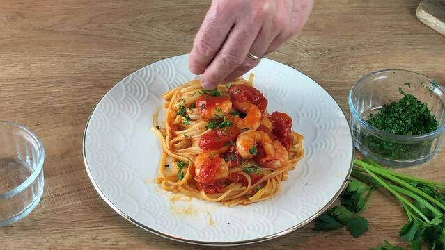 putting parsley over  Linguine with shrimp and cherry tomatoes