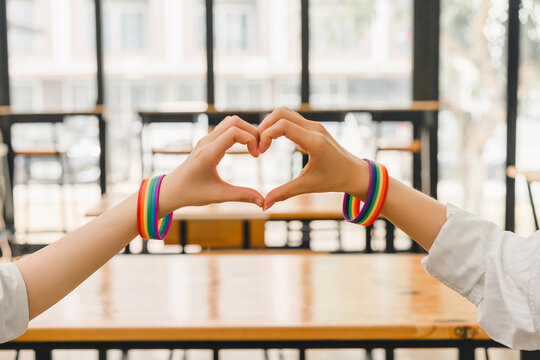 Two hands creating a heart symbol, showcasing rainbow bracelets in support of LGBTQ rights.