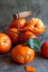 Ripe tangerines, tangerines with leaves and a cut out heart in a basket on a dark background.