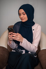 Muslim young woman using a phone while sitting on the sofa at home.