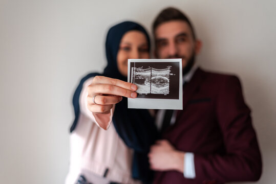 Gender Reveal Concept. Happy pregnant muslim couple holding holding baby ultrasound photo