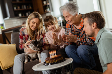 Joyous Family Celebrating Grandmothers Birthday With Cake in a Cozy Living Room - 760676384