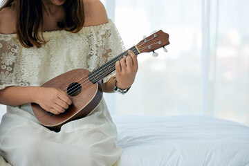 Fototapeta premium Close up young female Musician Playing Ukulele on a Bright Bedroom Morning