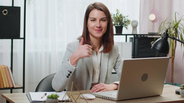Like. Happy Caucasian business woman looking approvingly at camera showing thumbs up sign positive something good great news positive feedback. Young pretty girl sitting at home office room at table.