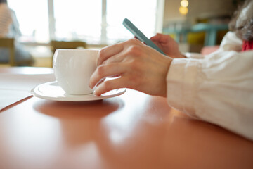 Woman drinking from white cup and using mobile phone