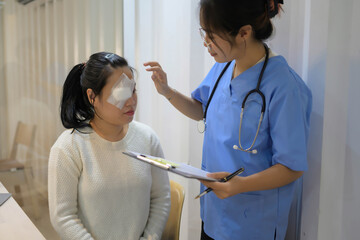 A woman with an eye patch sits in a chair while a nurse examines her