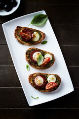 Crostini with tomato, salami and olive pesto on wooden background. Top view. Copy space, 