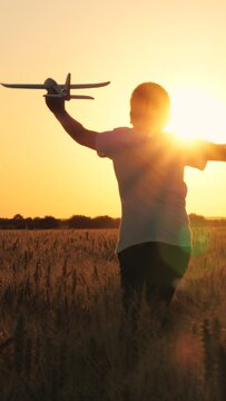 Cheerful boy teen running with plane toy on autumn wheat field at cinematic sunset sunrise back view closeup. Active male kid playing flying airplane plaything enjoy freedom happy childhood at meadow