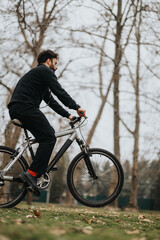 Obraz premium Active man on a casual bike ride in a park with bare trees in autumn.