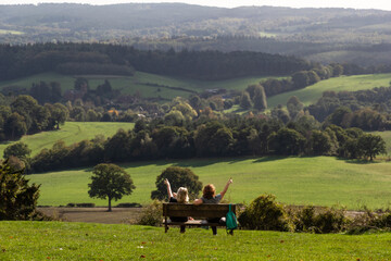 Two women friends sitting and chatting on a bench in the afternoon sun overlooking the beautiful...