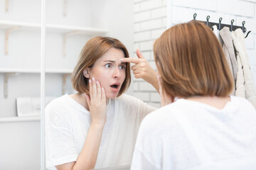 Young beautiful woman looking at mirror and confusing because of new wrinkles	
