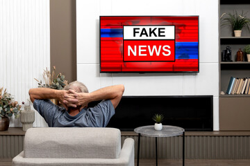 Elderly man watching Fake News on TV sitting on the couch at home	