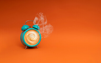 Hot coffee in a blue retro alarm clock on orange background. Waking up with alarm and coffee concept