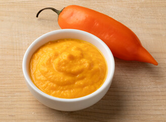 Fresh raw Peruvian Aji Amararillo pepper and a bowl with  Aji Amarillo sauce close up  