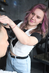 Barber using a hair dryer to clean the hair of a male client in a hair salon