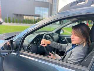 Caucasian middle-aged pretty concentrated woman driving own car going to work. Close up. Beautiful successful business lady sitting inside the auto looking at side mirror