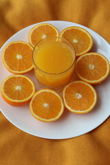  orange juice  and surrounding it are sliced halves of oranges arranged on the orange textured surface on plate