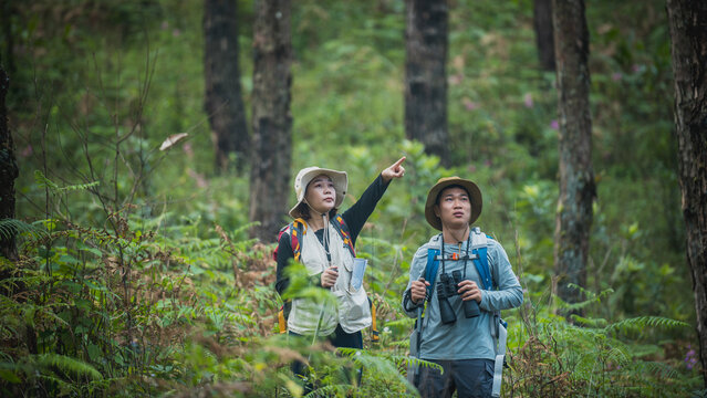 Attractive young couple hiking in the forest using binoculars.