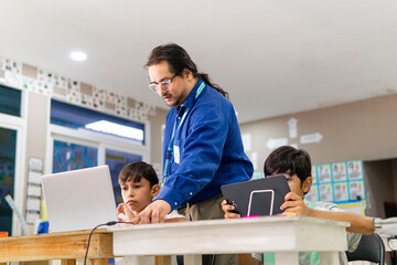 Teacher in class teaching student how use a laptop.