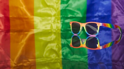 Rainbow sunglasses located on reflective plane and LGBT flag on background