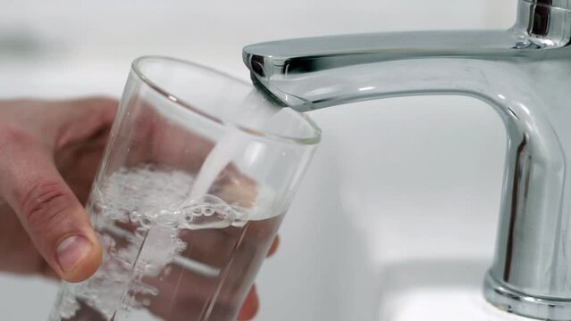 A man pours tap water into a glass glass. The concept of clean drinking water in a centralized water supply system.