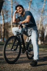 A happy man leans on his bike in a sunlit park, enjoying a leisurely outdoor activity on a clear day.
