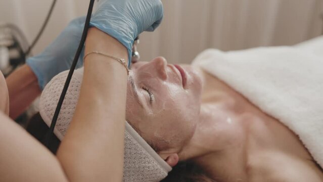 A beautician expertly using microcurrent facial treatment to a relaxed client in a serene spa setting, promoting skincare and wellness.