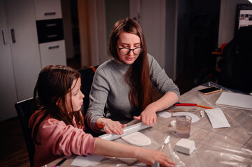 Intently focused, a mother assists her daughter with a clay craft project at home using rolling pin, showcasing a moment of shared concentration and educational interaction