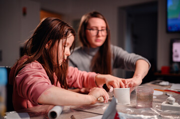 Fototapeta premium A girl and a woman are absorbed in creating a craft with clay, a dynamic scene of family interaction and joint creativity at home