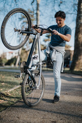 A cheerful man enjoys outdoor recreation by lifting his mountain bike in a park with trees in the background.