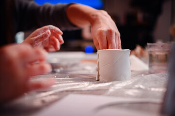 A child's hands carefully construct a clay house, with the focused guidance of a parent,...