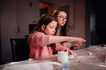 The sheer delight of a girl sculpting with clay is shared with her mother, capturing the essence of joyous learning and creative expression within the family